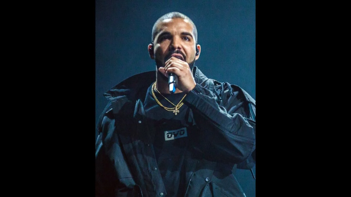 Drake performing live on stage holding a microphone in a black jacket