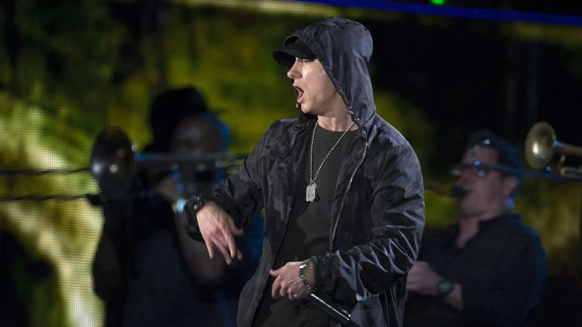 Eminem performing live on stage wearing a dark hooded jacket and cap