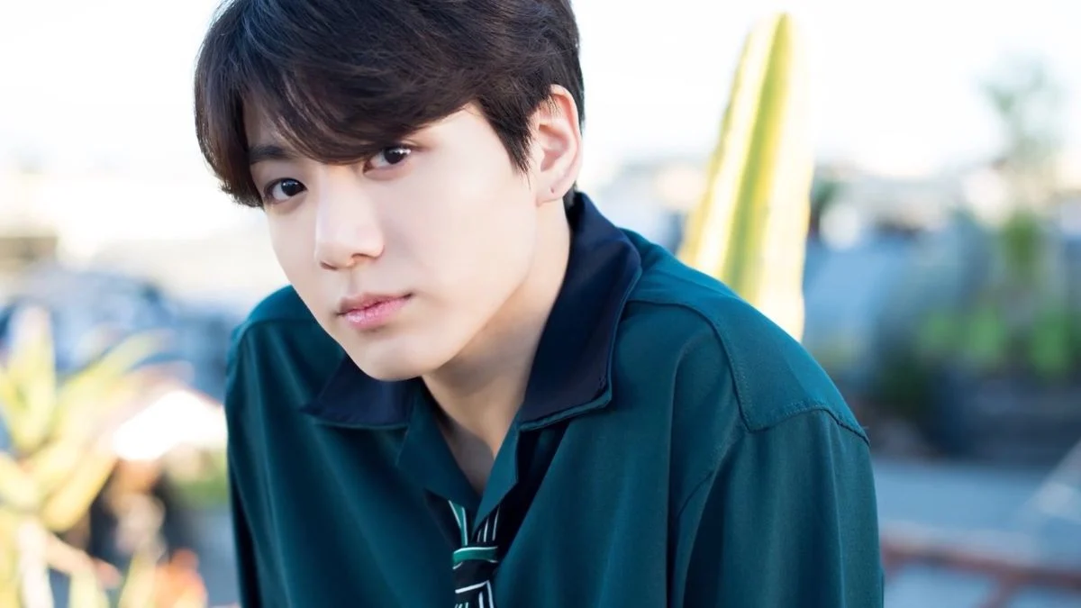 BTS member Jungkook looking at the camera wearing a dark green shirt outdoors