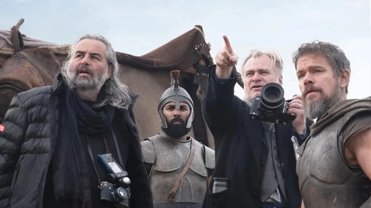 Director Christopher Nolan pointing on location alongside producer Emma Thomas and actor Matt Damon in costume for The Odyssey