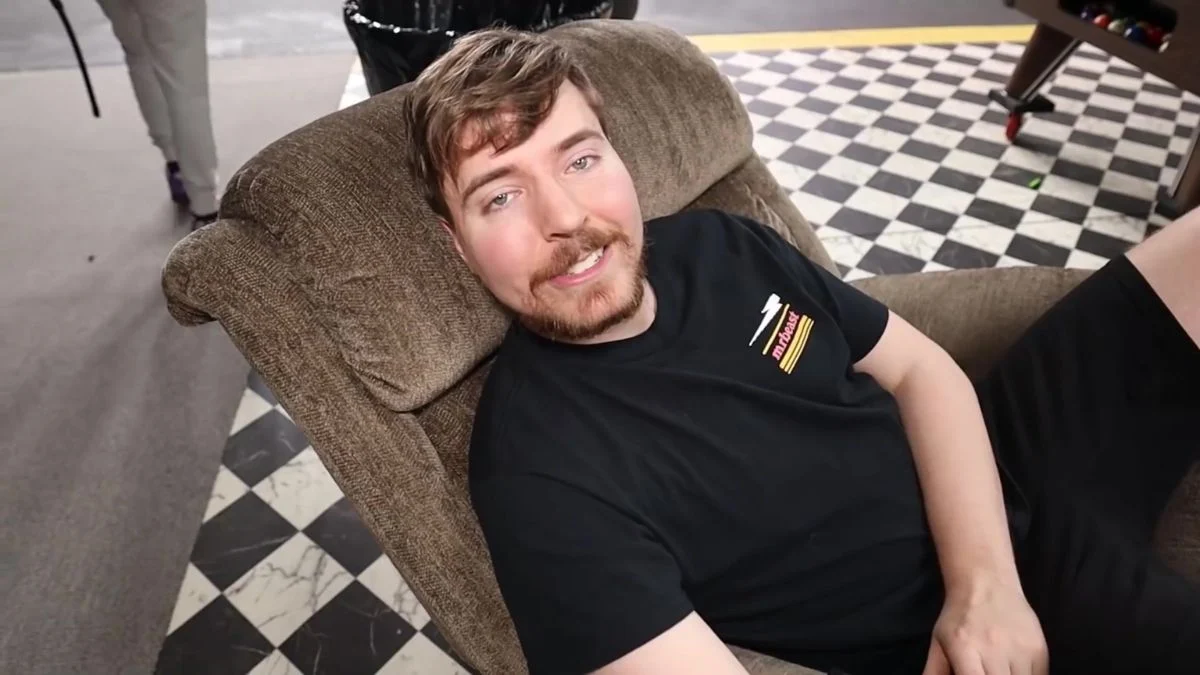 Jimmy Donaldson, known as MrBeast, wearing a black logo t-shirt and reclining in an armchair.