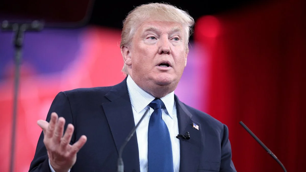 Donald Trump gesturing with his hand while speaking at a podium in a navy suit and tie