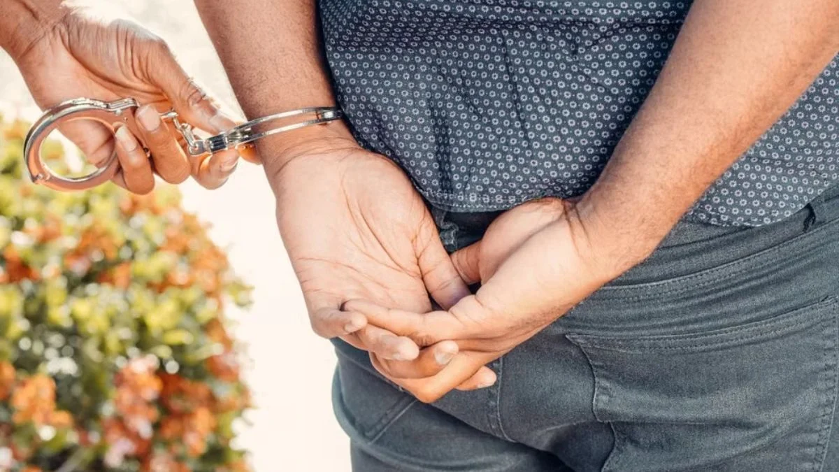 A person being handcuffed outdoors with hands behind their back
