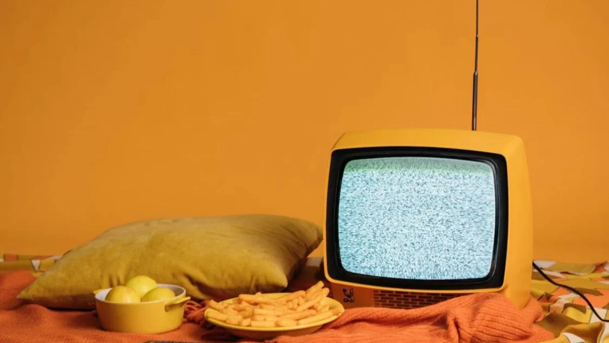 Small retro yellow television set with static on the screen next to snacks on a table