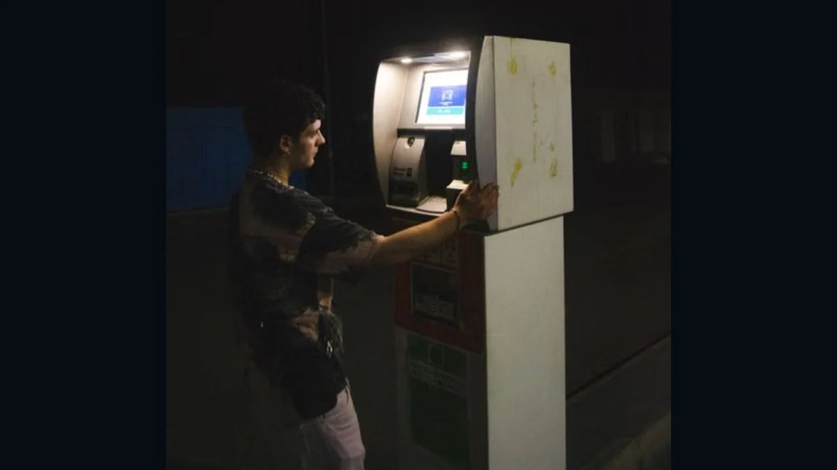 A man using an outdoor automated teller machine (ATM) terminal at night.