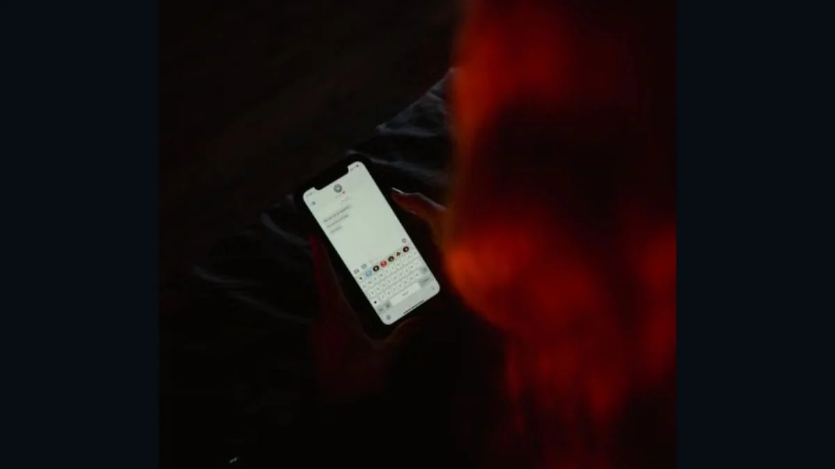 Over the shoulder view of a person holding a smartphone and typing text messages in dim lighting.