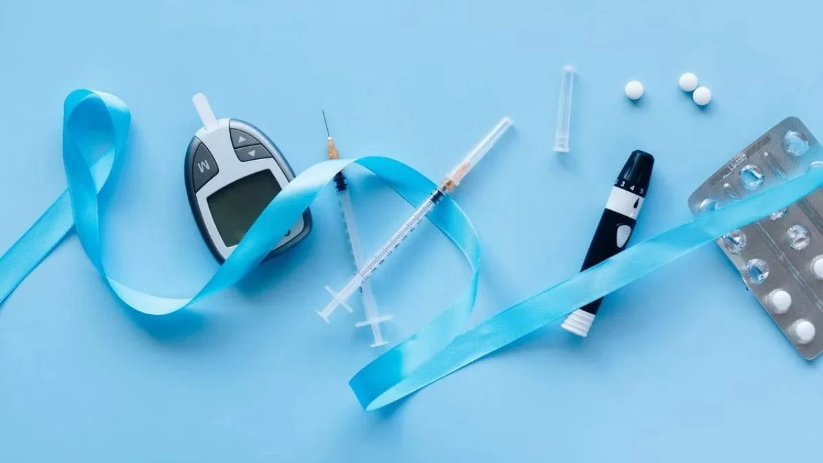 Diabetes testing equipment including a blood glucose meter, lancing device, insulin syringes, and a blue awareness ribbon on a light blue background.