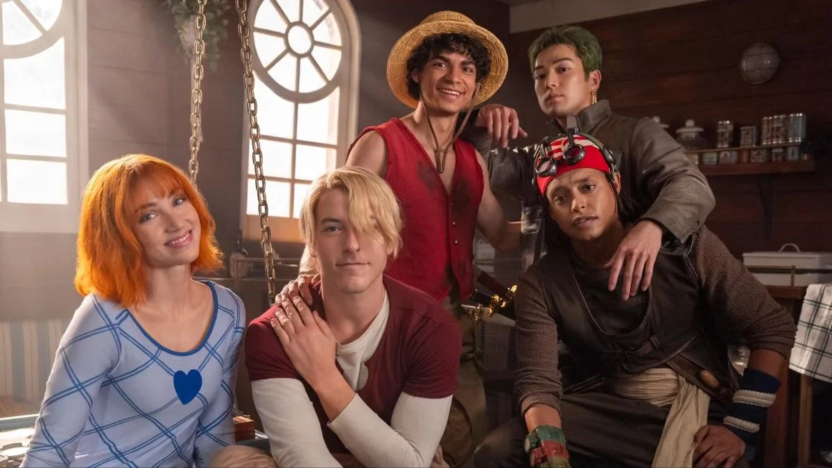 The main cast of Netflix's live-action One Piece—Emily Rudd, Taz Skylar, Iñaki Godoy, Mackenyu, and Jacob Romero—smiling together onboard the Going Merry.
