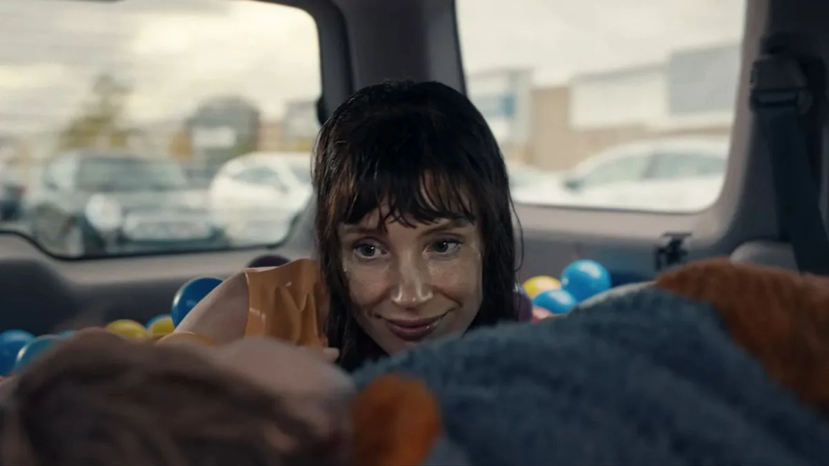 Jessica Chastain with dark bangs and a wide smile looking at a child in the back seat of a vehicle filled with plastic balls.