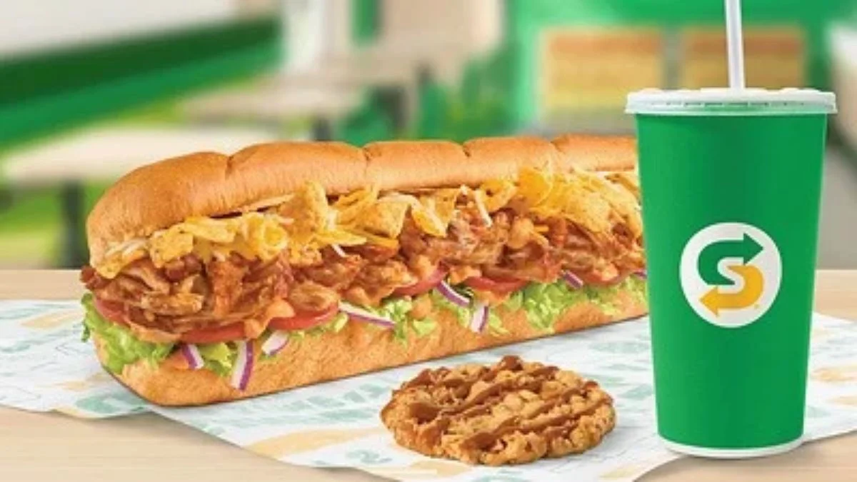 Subway Footlong Fritos Chicken Enchilada Sub next to a Caramel Apple Cookie and a green Subway cup
