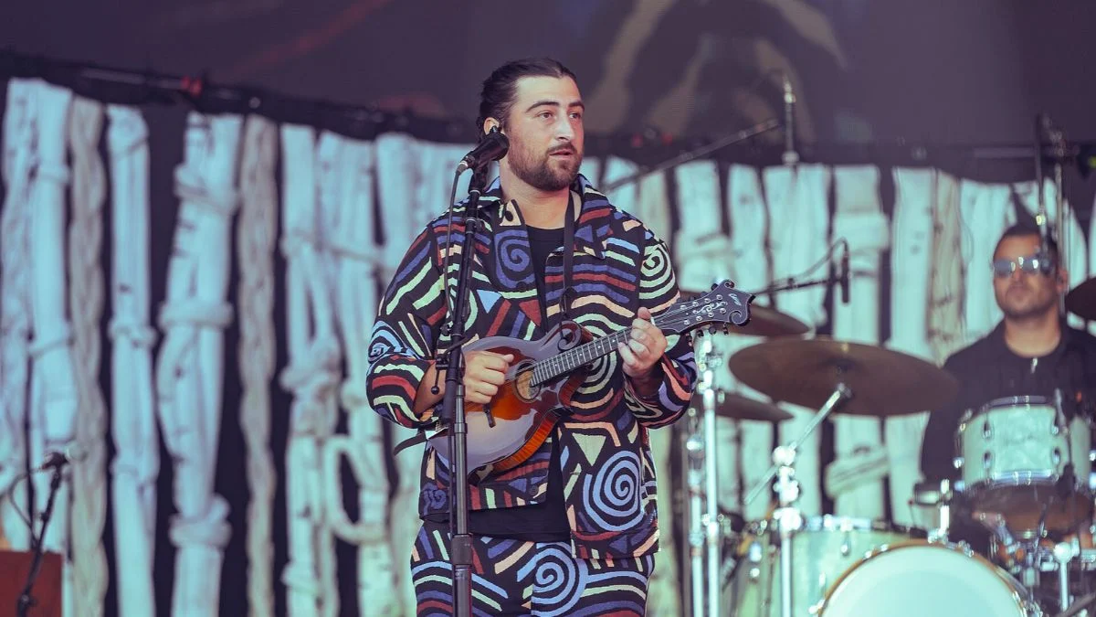 Noah Kahan playing mandolin on stage in a patterned jacket during a live performance