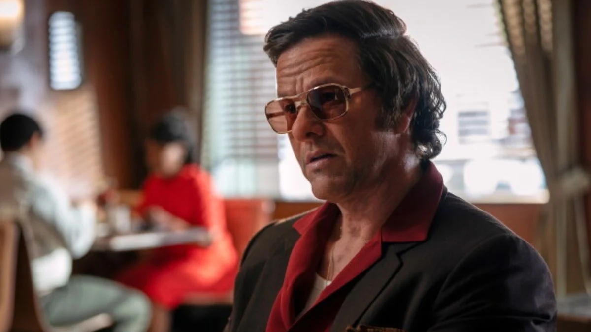 Mark Wahlberg wearing sunglasses and a red shirt in a scene from the crime drama By Any Means