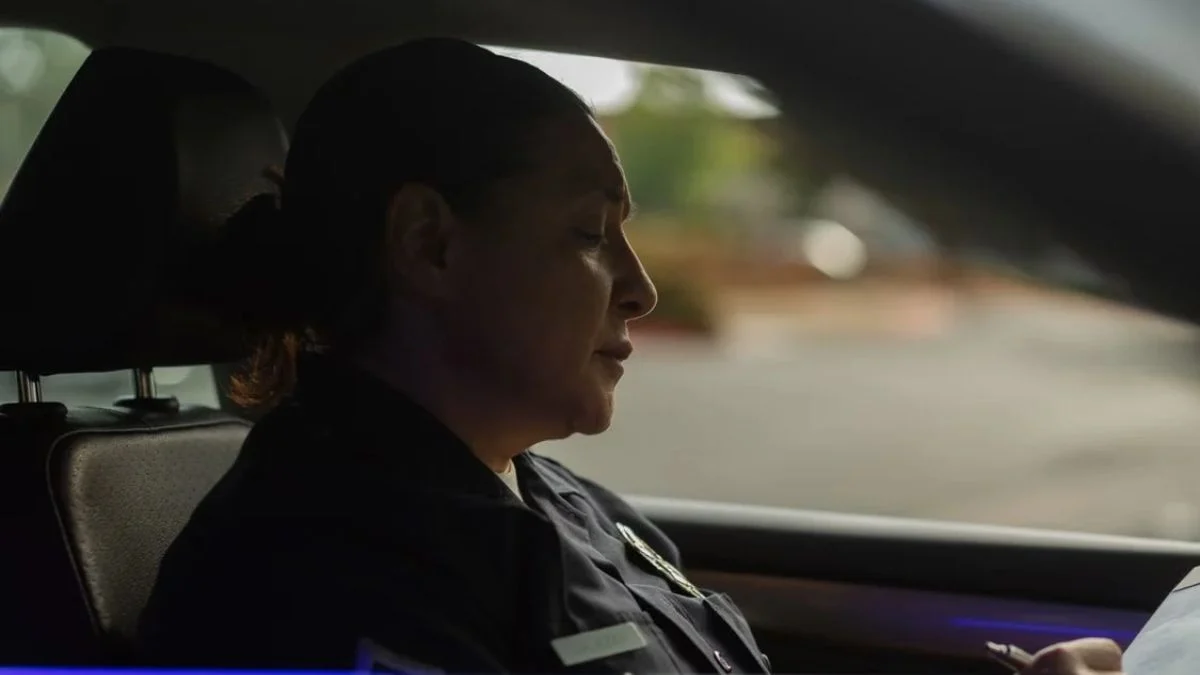 Side profile of a female police officer sitting inside a patrol car looking down at paperwork.